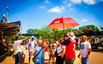Tour group exploring San Basilio de Palenque market, Cartagena, with guide under red umbrella.