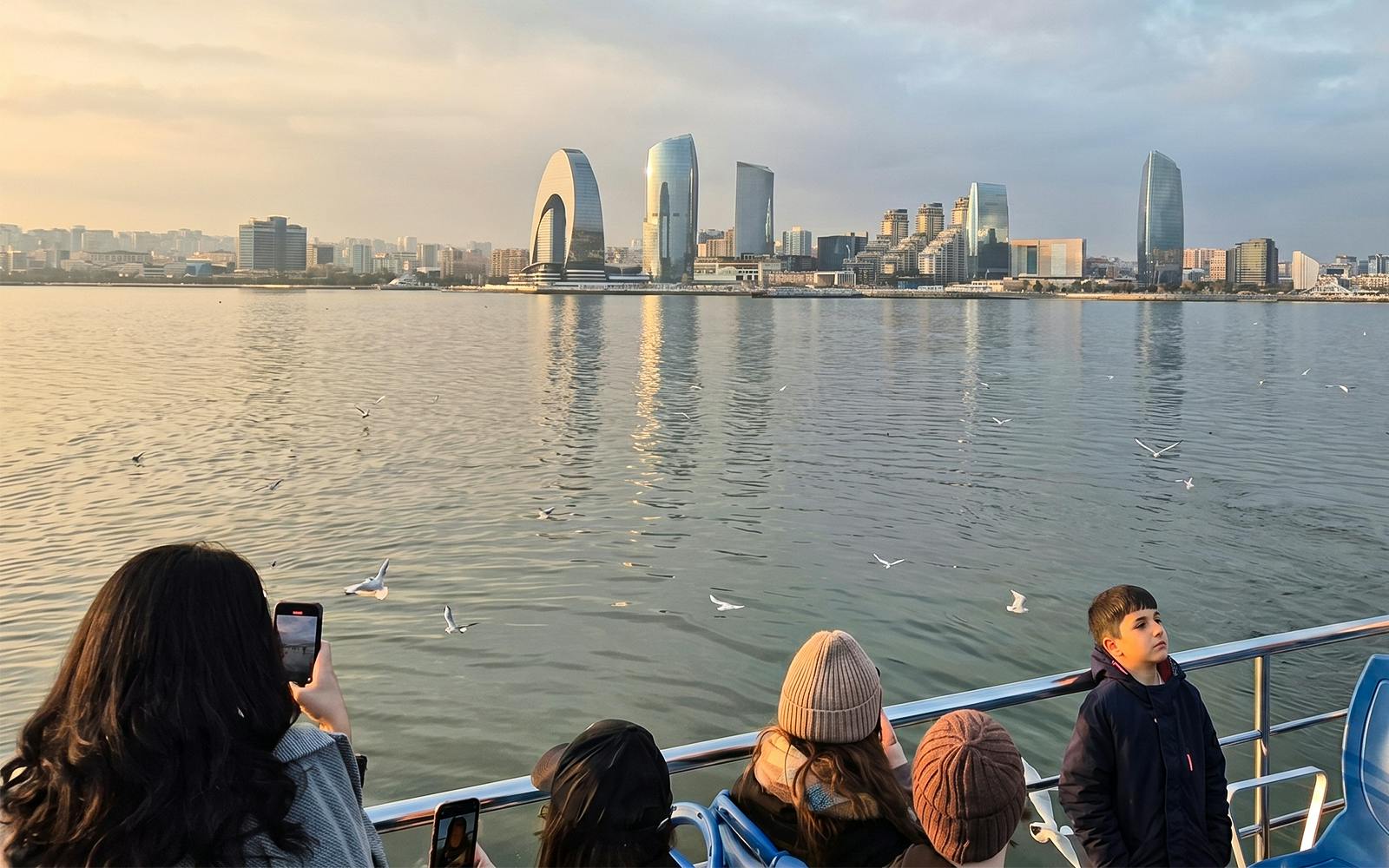 Baku skyline from Caspian Sea boat tour with tourists and seagulls.