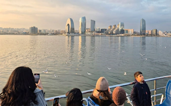 Baku skyline from Caspian Sea boat tour with tourists and seagulls.