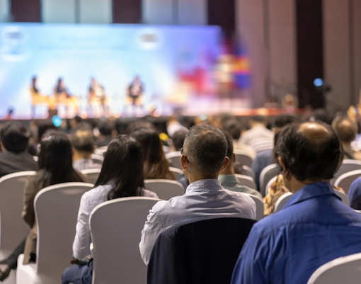 Audience attending a conference with speakers on stage.
