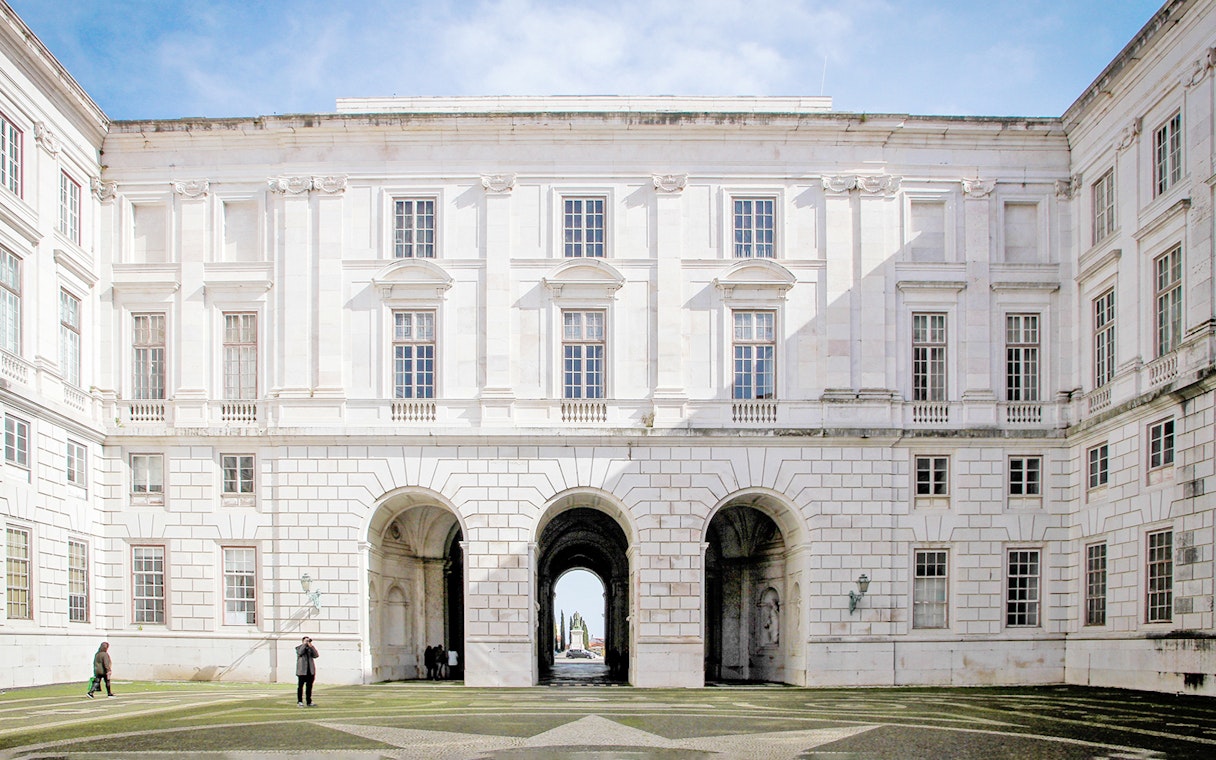 Courtyard of National Palace of Ajuda, Lisbon with arched entrance and visitors.