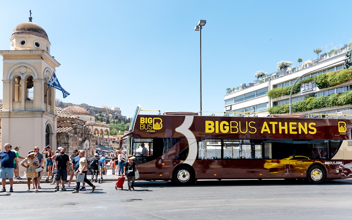Athens hop-on hop-off bus near historical landmarks under blue skies.