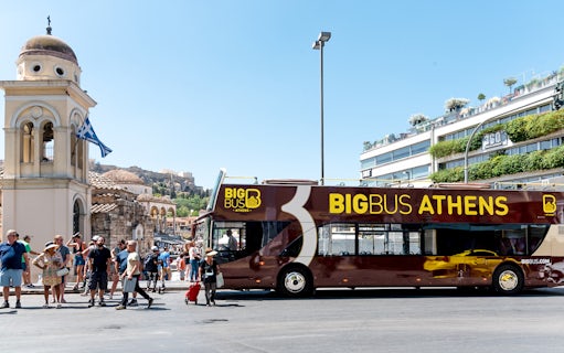 Athens hop-on hop-off bus near historical landmarks under blue skies.