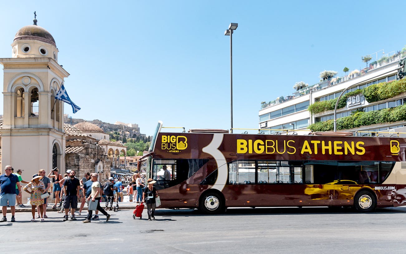 Athens hop-on hop-off bus near historical landmarks under blue skies.