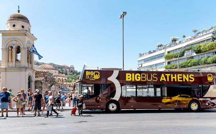 Athens hop-on hop-off bus near historical landmarks under blue skies.