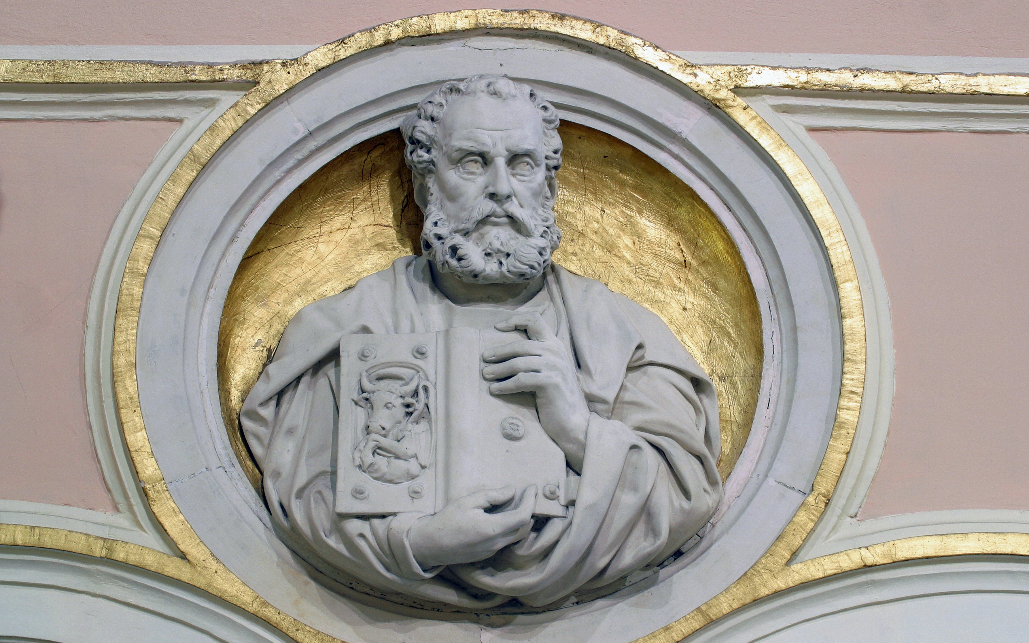 Relief sculpture of Saint Luke the Evangelist holding a book with a bull emblem.