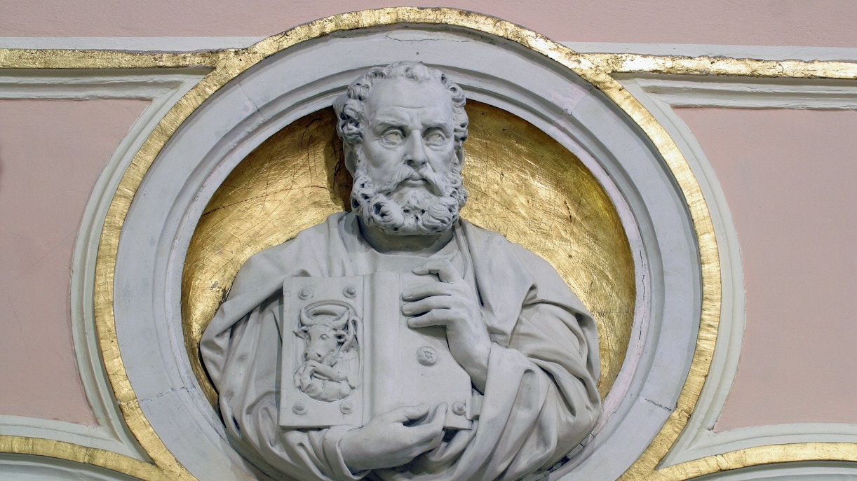 Relief sculpture of Saint Luke the Evangelist holding a book with a bull emblem.