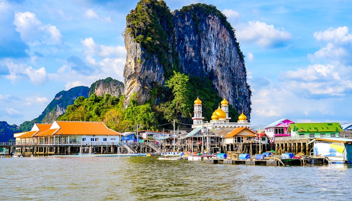 Floating fishing village of Koh Panyee with limestone cliff and colorful buildings.