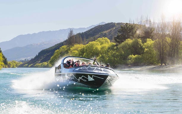 Jet boat speeding on Kawarau River with passengers enjoying the ride.