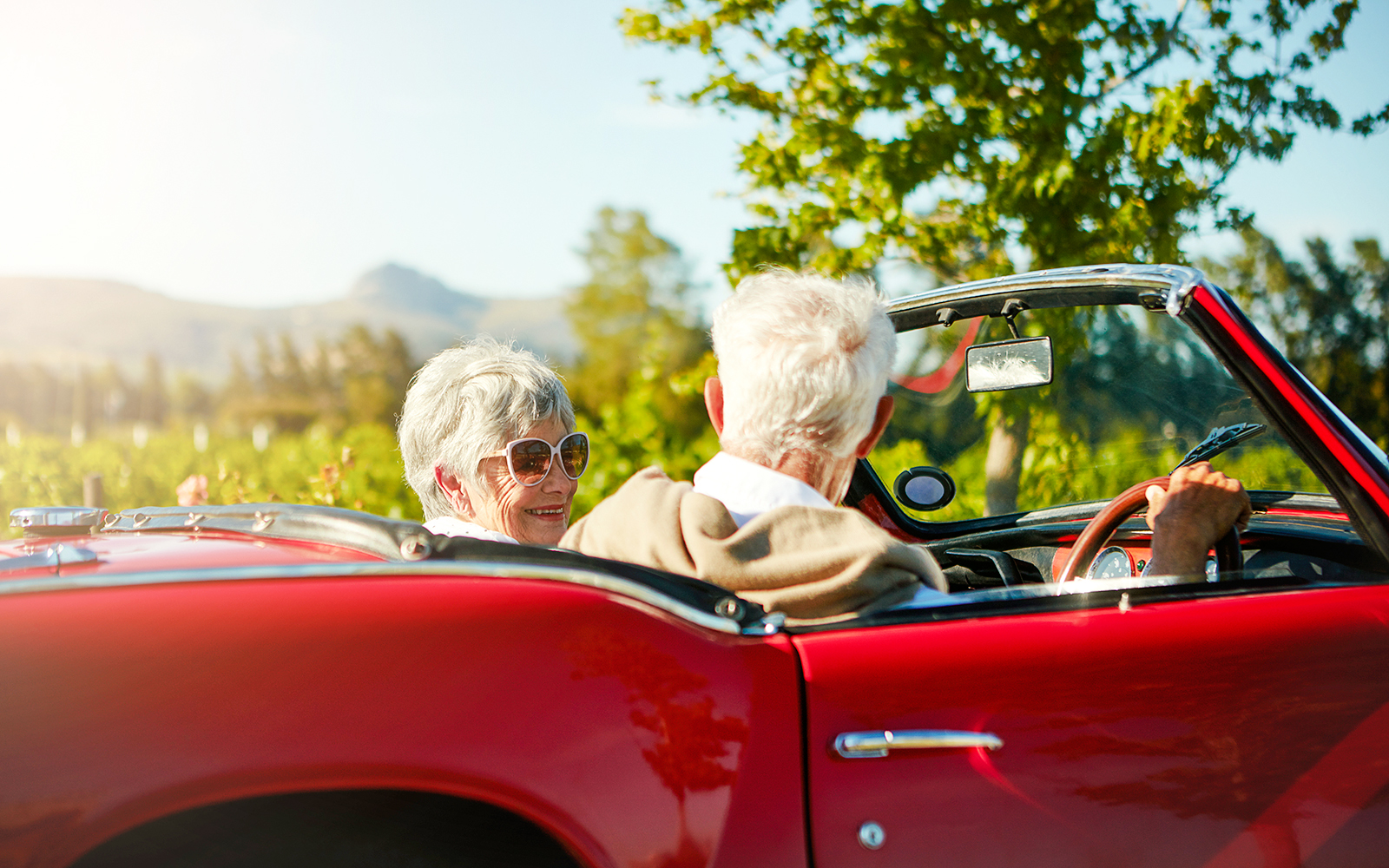 Couple driving a red convertible through the countryside towards Chenonceau Castle.