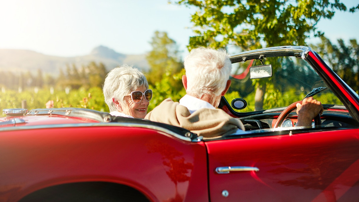 Couple driving a red convertible through the countryside towards Chenonceau Castle.