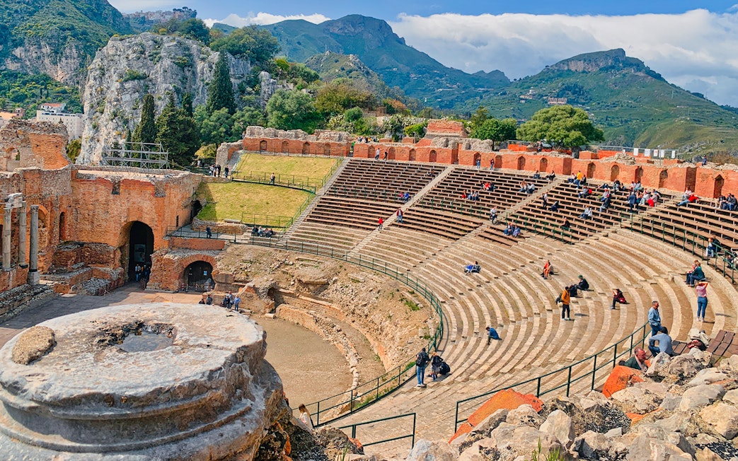 Ancient Theater of Taormina with visitors seated on stone steps, Sicily.
