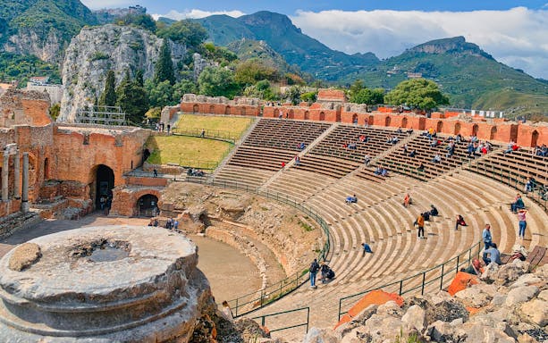 Ancient Theater of Taormina with visitors seated on stone steps, Sicily.