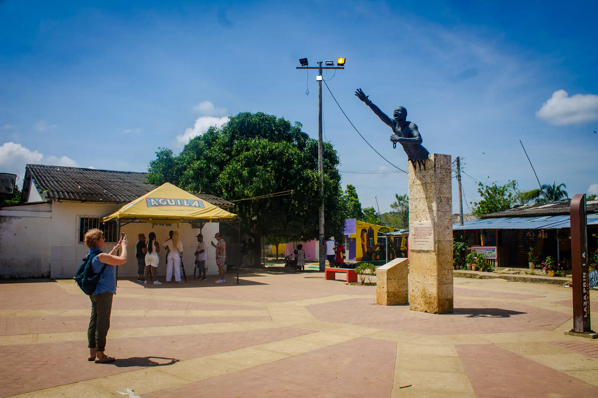 Statue in San Basilio de Palenque square with tourists and local market, Cartagena tour.