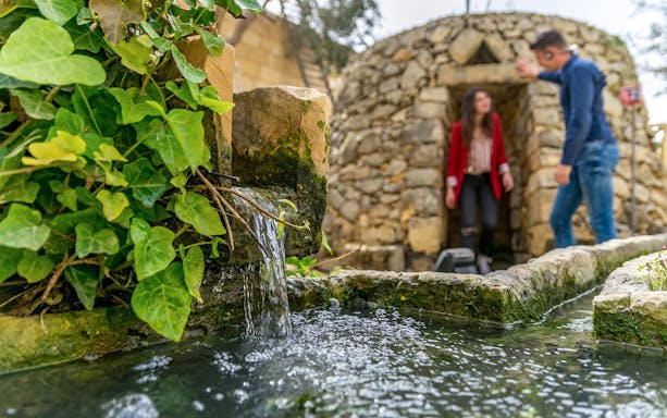 Stone structure with flowing water and visitors at prehistoric temple site.