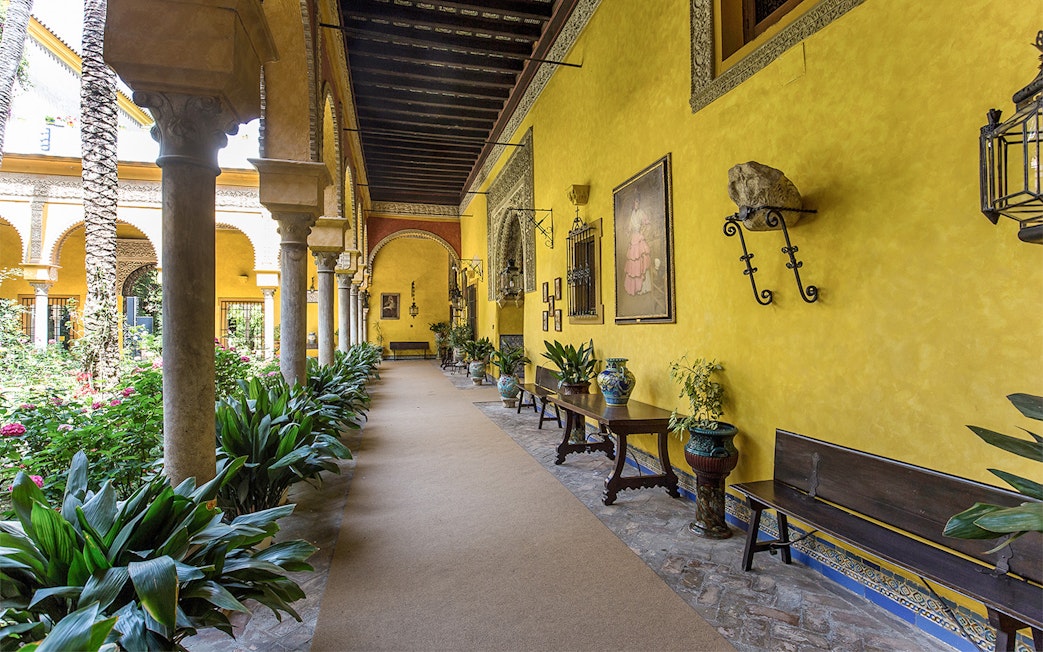 Palacio de las Dueñas courtyard with yellow walls, arches, and lush greenery.