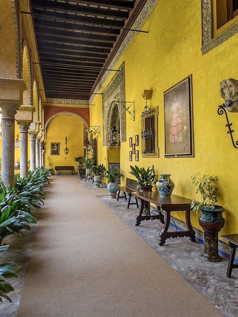 Palacio de las Dueñas courtyard with yellow walls, arches, and lush greenery.