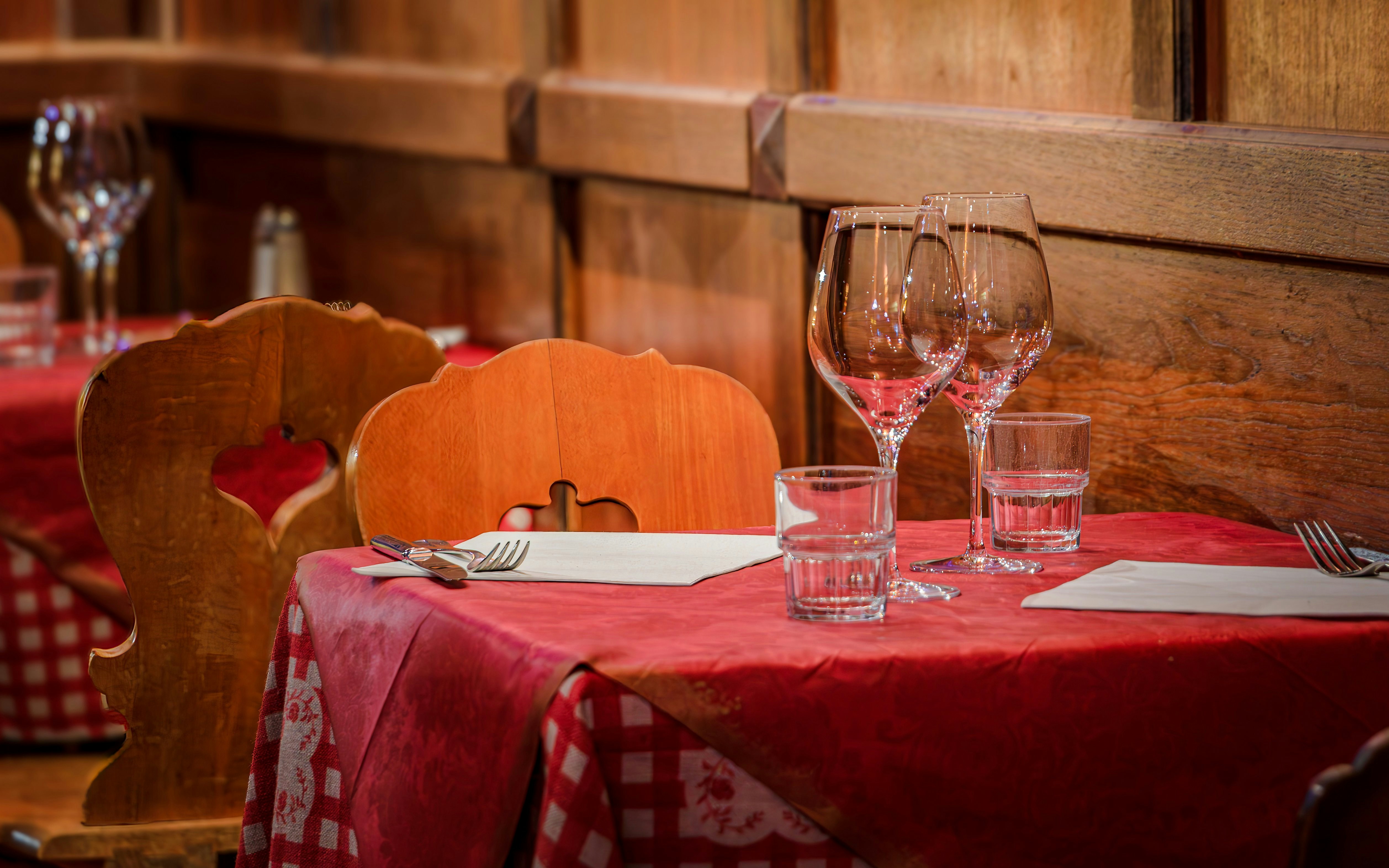 Restaurant table set with red tablecloth, wine glasses, and wooden chairs.