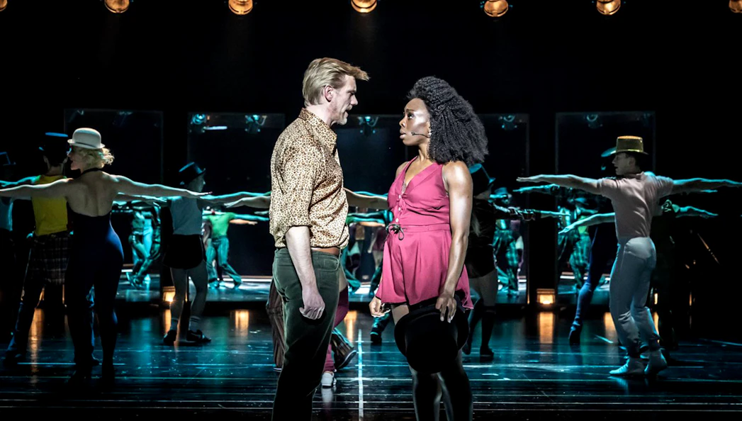 Performers on stage during "A Chorus Line" musical, with dancers in the background.