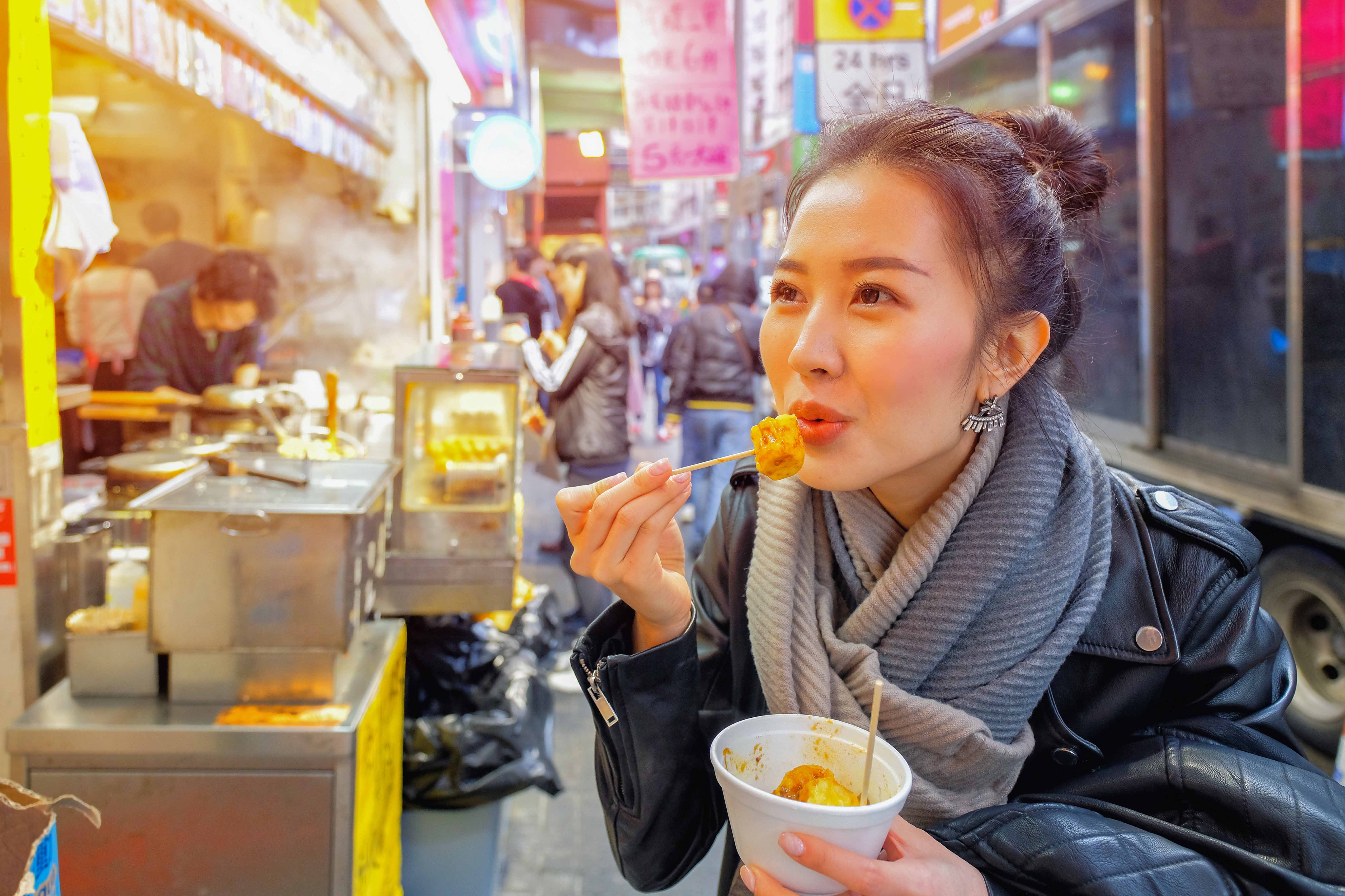 Woman enjoying dumplings at a Hong Kong street food stall.