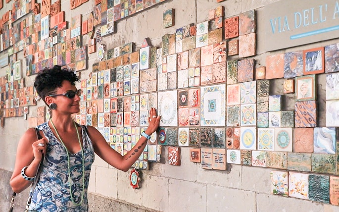 Woman admiring colorful tiles on a wall in Via dell'Arte, Italy.