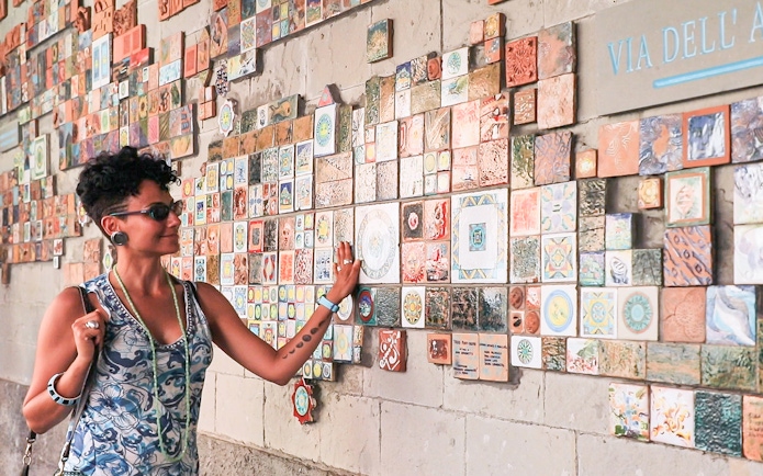 Woman admiring colorful tiles on a wall in Via dell'Arte, Italy.