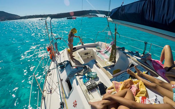 Sailboat deck with people relaxing, turquoise waters of Asinara National Park, Stintino excursion.