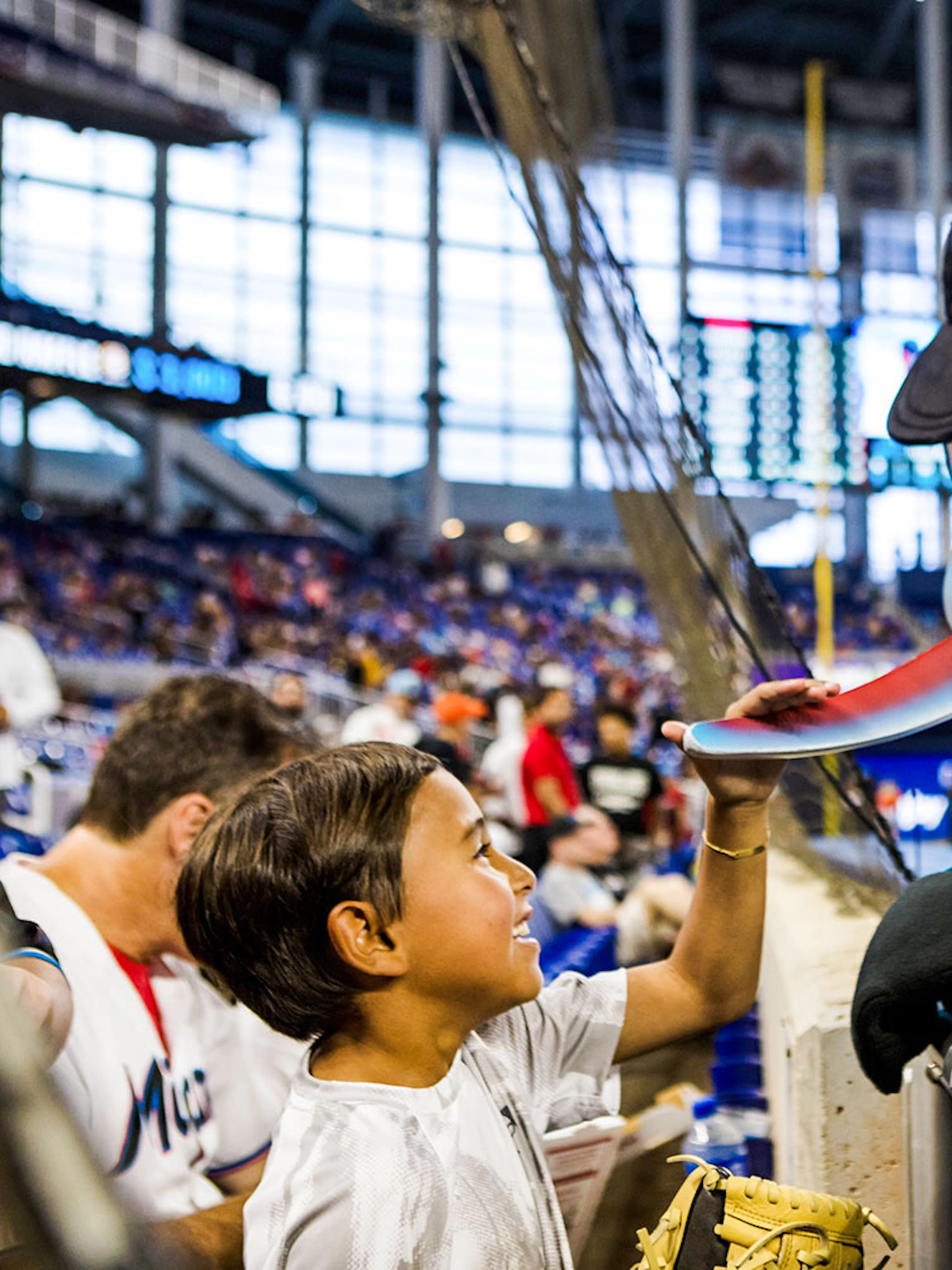 Child interacting with Miami Marlins mascot at baseball game in Miami stadium.