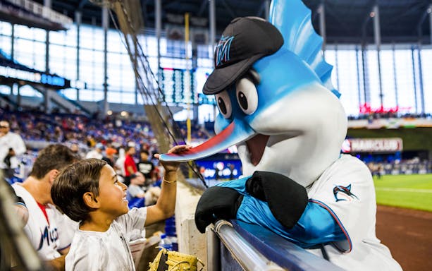 Child interacting with Miami Marlins mascot at baseball game in Miami stadium.