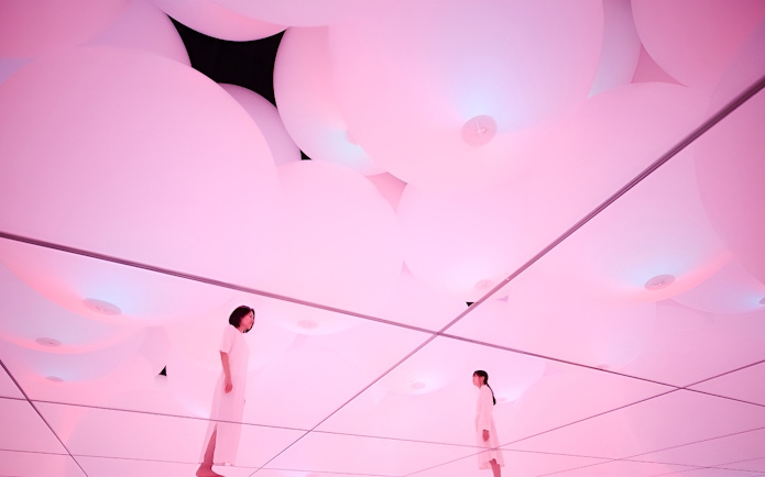 Visitors in mirrored room with pink digital light at TeamLab Planets Tokyo exhibit.