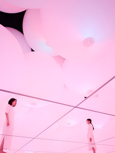 Visitors in mirrored room with pink digital light at TeamLab Planets Tokyo exhibit.
