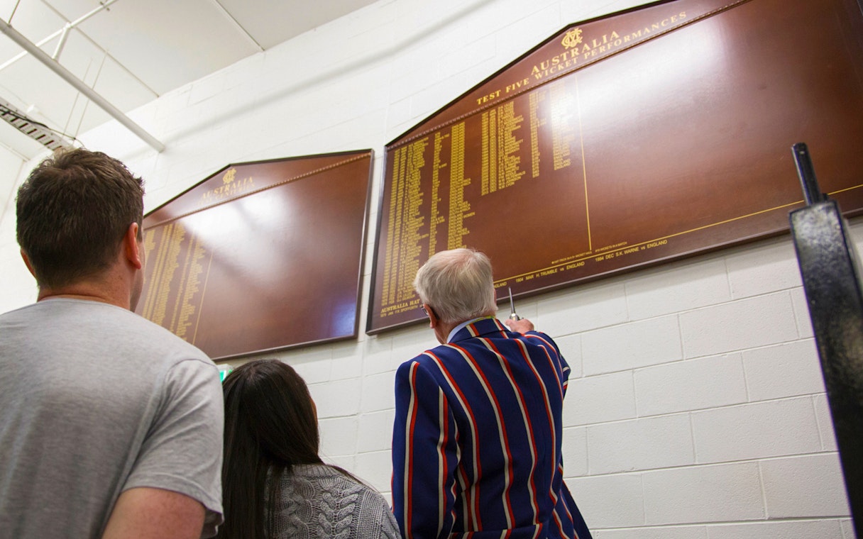Visitors viewing cricket honors board during Melbourne MCG Stadium tour.