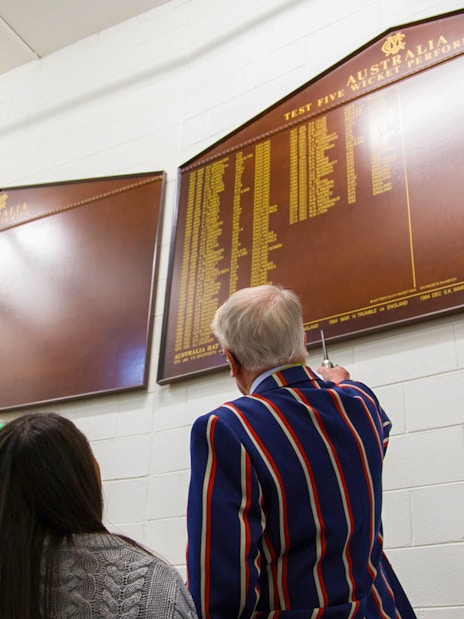 Visitors viewing cricket honors board during Melbourne MCG Stadium tour.