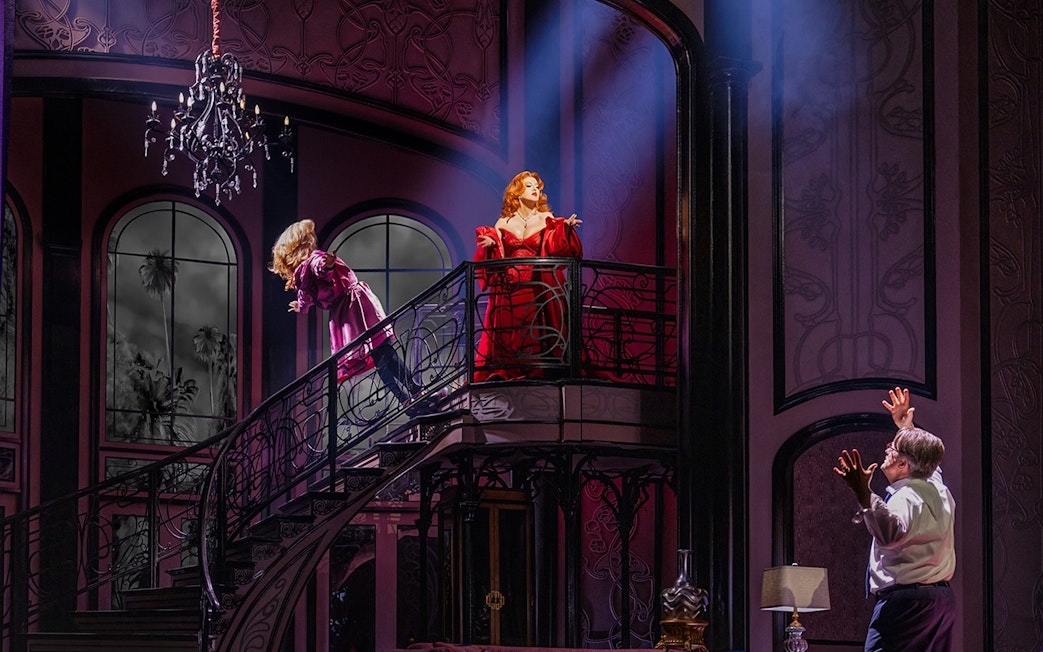 Two actors on a grand staircase in a dramatic scene from "Death Becomes Her" stage production.