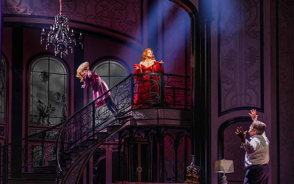 Two actors on a grand staircase in a dramatic scene from "Death Becomes Her" stage production.