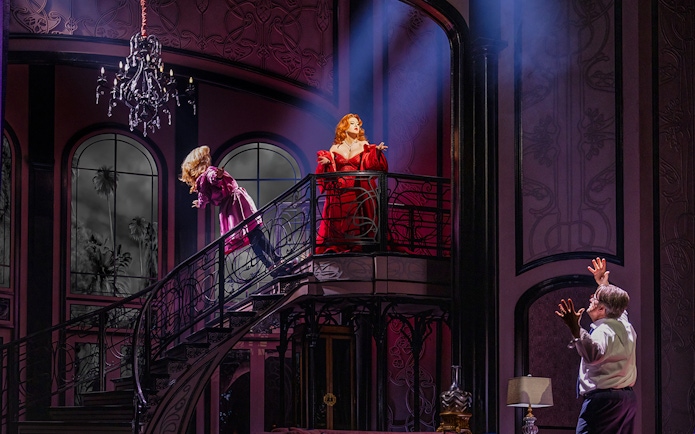 Two actors on a grand staircase in a dramatic scene from "Death Becomes Her" stage production.
