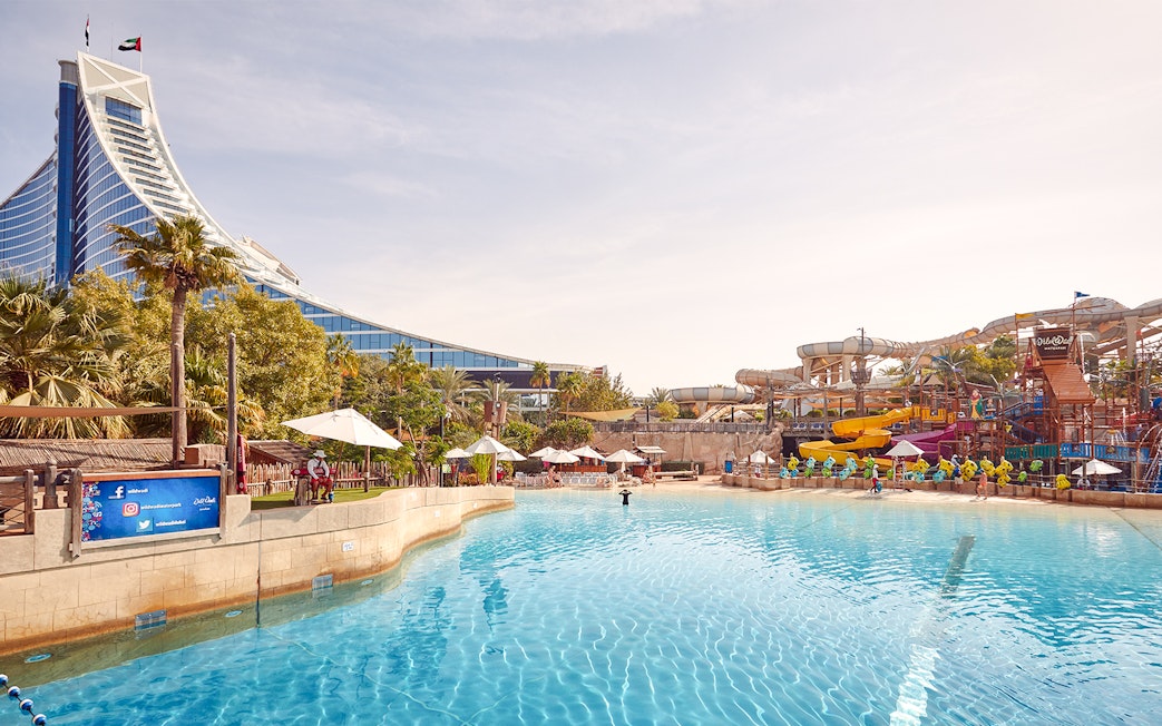 Visitors enjoying water rides at Wild Wadi Water Park, Dubai, with Jumeirah Beach Hotel in the background.