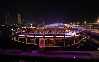 Dhow cruise with dining guests on Dubai Marina at night, city skyline in background.
