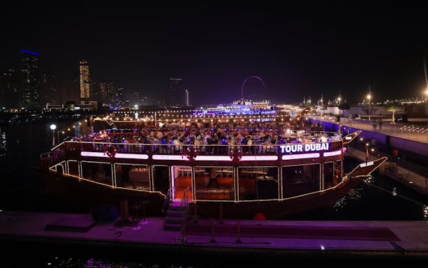 Dhow cruise with dining guests on Dubai Marina at night, city skyline in background.