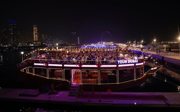 Dhow cruise with dining guests on Dubai Marina at night, city skyline in background.