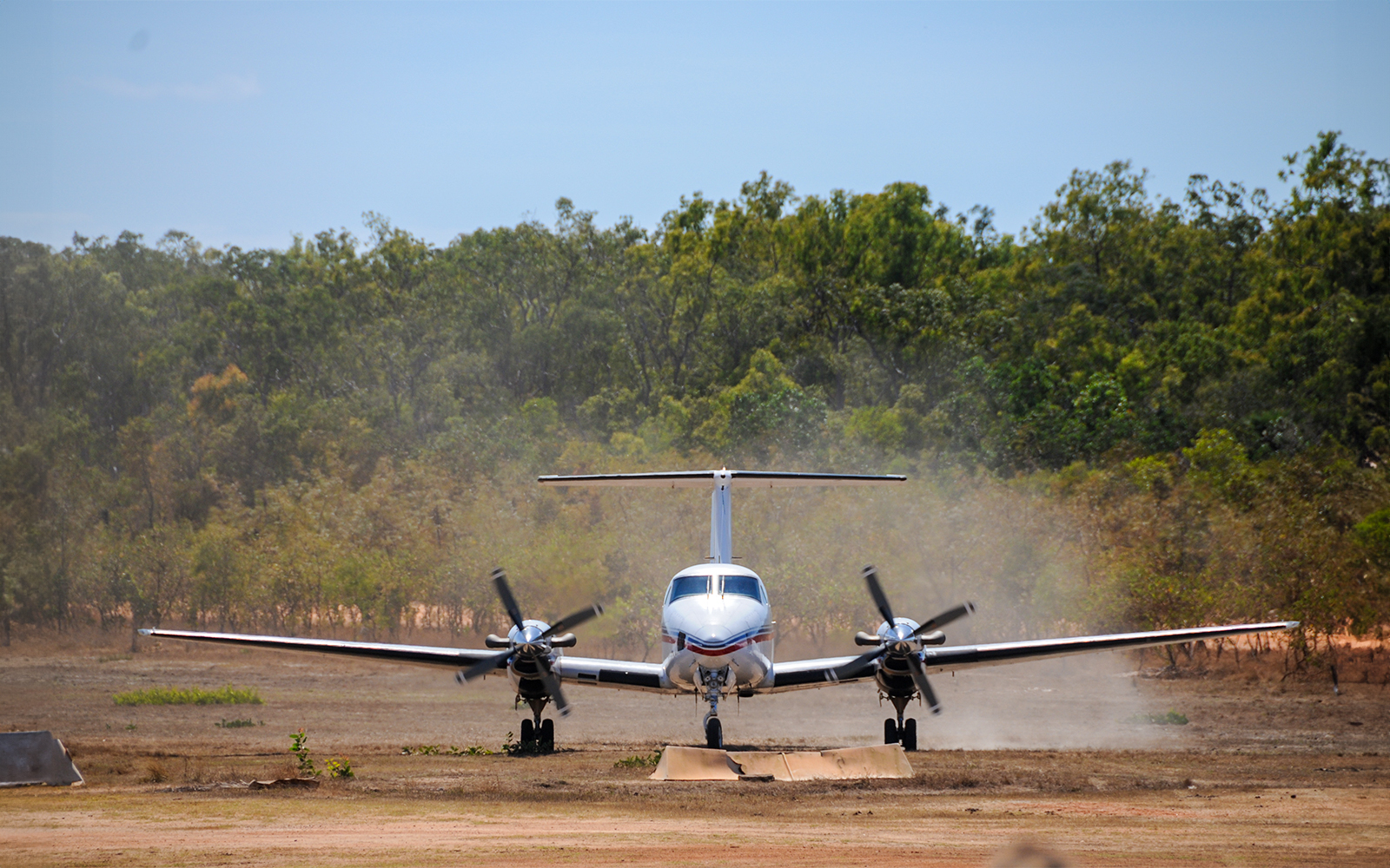 Small aircraft landing on a dirt runway surrounded by trees, part of Royal Flying Doctor Service tour.