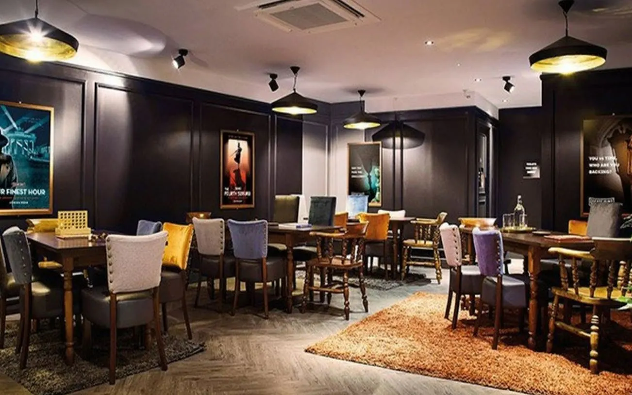 Escape room interior with tables and chairs, Alice in Puzzleland Dubai posters on walls.