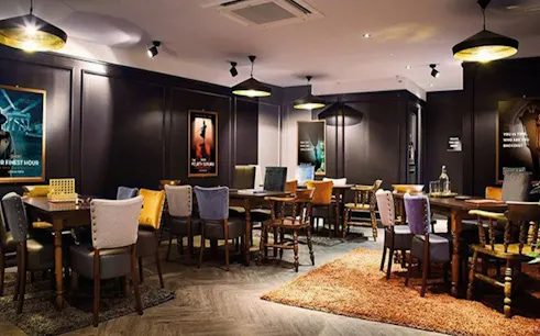 Escape room interior with tables and chairs, Alice in Puzzleland Dubai posters on walls.