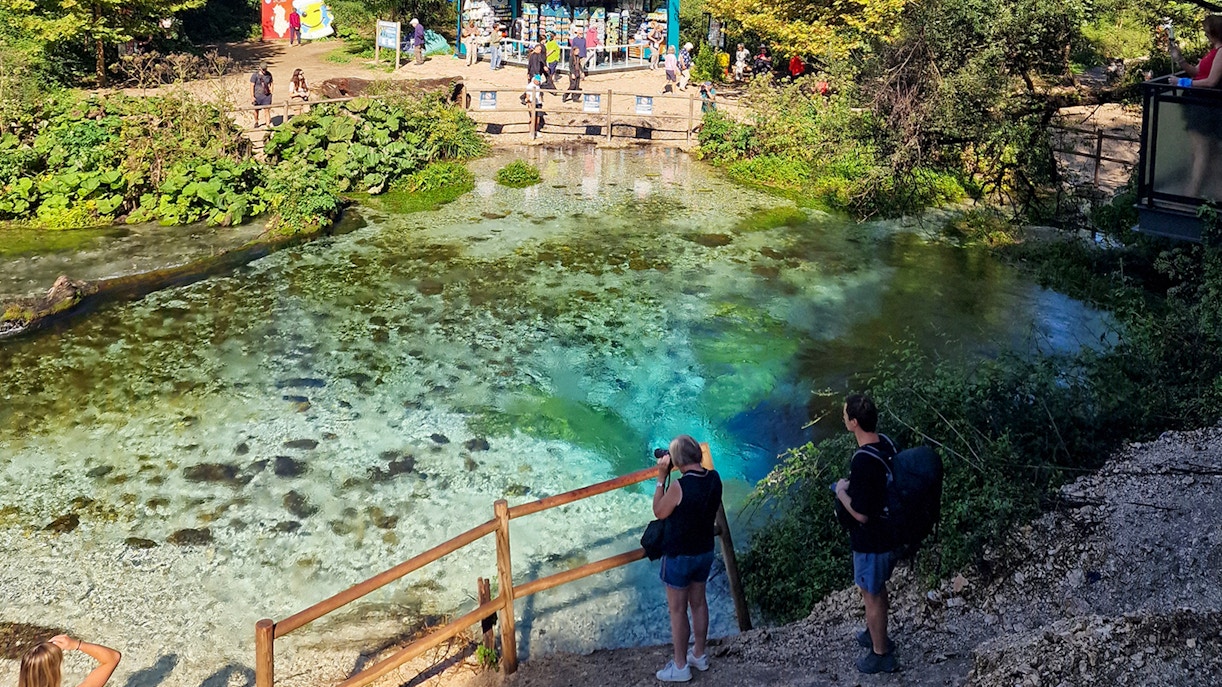 Visitors observing the Blue Eye spring in Albania with vibrant turquoise water.