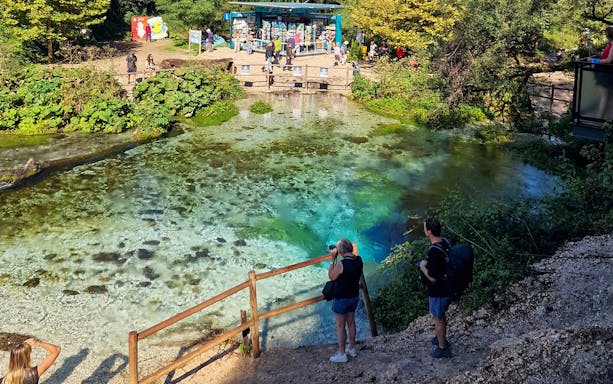 Visitors observing the Blue Eye spring in Albania with vibrant turquoise water.