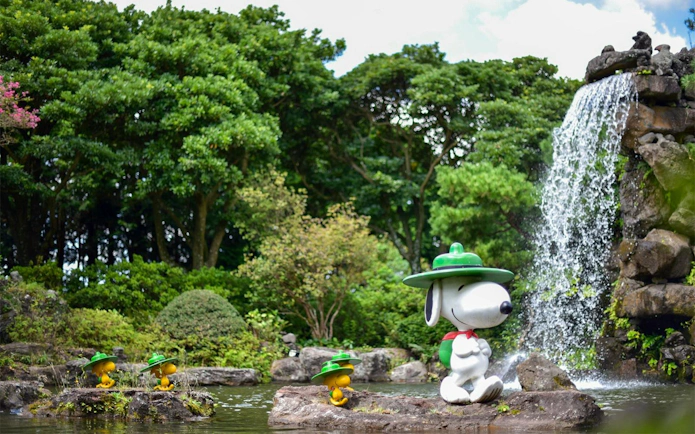 Snoopy statue by waterfall in Snoopy Garden, Jeju Island, surrounded by lush greenery.