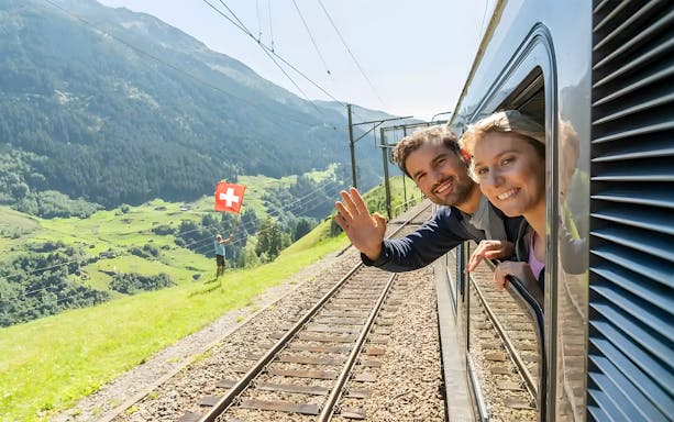 Passengers on Gotthard Panorama Express train enjoying Swiss Alps view.