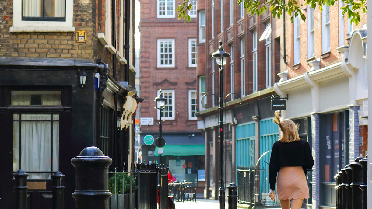 Woman walking down a street in Soho, London at sunset.