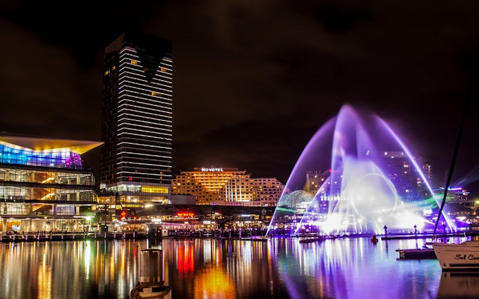 Sydney Darling Harbour night view with colorful lights and water fountain during Vivid 2022 Cruise.