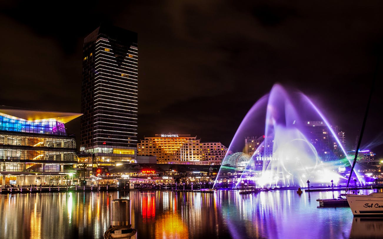 Sydney Darling Harbour night view with colorful lights and water fountain during Vivid 2022 Cruise.